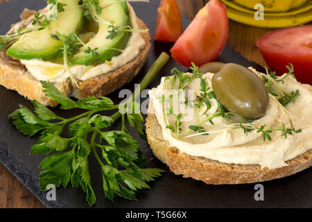 Hummus Sandwiches mit Avocado und Micro Rucola Sprößlinge auf schwarzem Granit board Stockfoto