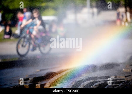 Berlin, Deutschland. 24 Apr, 2019. Ein Junge reitet auf seinem Fahrrad hinter dem Brunnen im Lustgarten, wo ein Regenbogen im Wasser Nebel gesehen werden kann. Credit: Christoph Soeder/dpa/Alamy leben Nachrichten Stockfoto