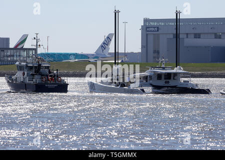 Hamburg, Deutschland. 25 Apr, 2019. Die Wasserstoff-betriebenen Schiff 'Beobachter' wird auf der Elbe neben dem Zoll Schiff "glückstadt" bei der Ankunft Segel im Hamburger Hafen. Das Airbus-werk in Hamburg-Finkenwerder kann im Hintergrund gesehen werden. Der Katamaran ist 30 Meter lang und fast 13 Meter breit, ist in der Lage, seine eigenen Wasserstoff aus Meerwasser zu produzieren und damit arbeitet ohne den Ausstoß von Treibhausgasen oder Feinstaub. Credit: Bodo Marks/dpa/Alamy leben Nachrichten Stockfoto