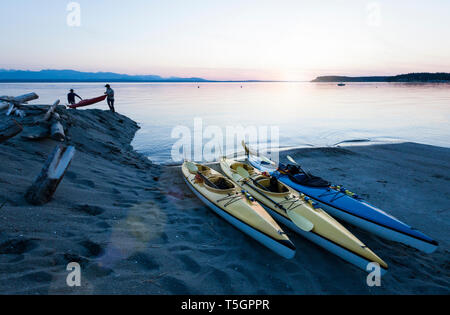 Menschen Männer Freunde Kajakfahren im Meer, die Boote am Strand bei Sonnenuntergang. Whidbey Island, Washington, United States Abenteuer im freien Wasser Sport reisen. Stockfoto