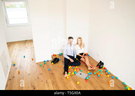 Business Paar sitzen auf dem Boden ihrer neuen Heimat mit bunten Kugeln Stockfoto