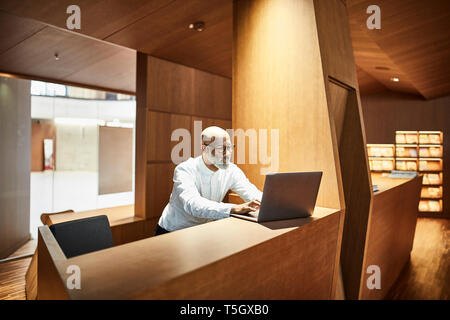 Reifer mann Arbeiten am Laptop am Arbeitsplatz in der Bibliothek Stockfoto