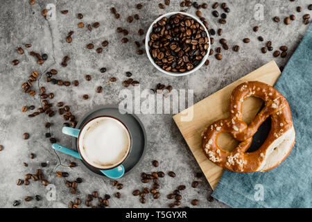 Tasse Kaffee, Kaffeebohnen und Brezel auf Serviette und Holzbrett Stockfoto