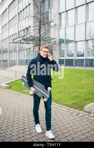 Lächelnden jungen Mann mit Skateboard Gespräch am Handy in der Stadt Stockfoto