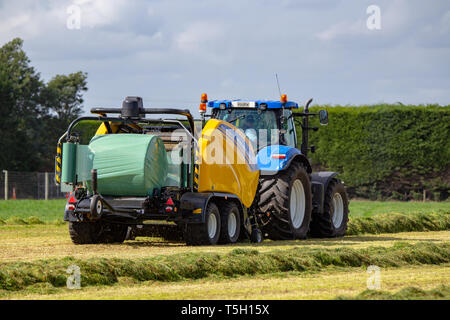 Kirwee, Canterbury, Neuseeland, 27. März 2019: Ein New Holland ballen Wrapper und Traktor am Arbeitsplatz, Heuballen, Südinsel landwirtschaftliches Feld Tage Stockfoto