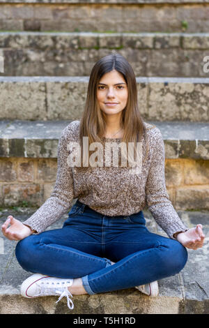 Junge Frau sitzt im Freien auf Treppen Yoga Stockfoto