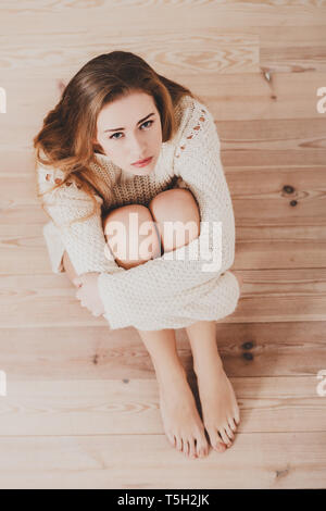Deprimiert junge Frau auf Holzboden zu Hause sitzen, Ansicht von oben. Stockfoto