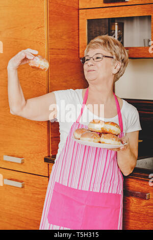 Ältere Frau hält Teller mit Haufen Donuts in der Küche. Stockfoto