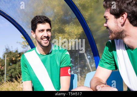 Zwei glückliche Fußball Spieler sitzt auf der Bank am Fußball Feld sprechen Stockfoto