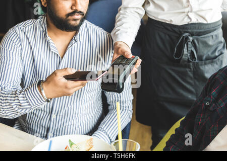 Junge attraktive hinduistischen Mann Bezahlen im Café mit berührungsloser smartphone Zahlung Stockfoto