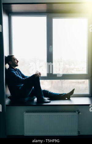 Hübscher junger Mann sitzt auf Fensterbank Stockfoto