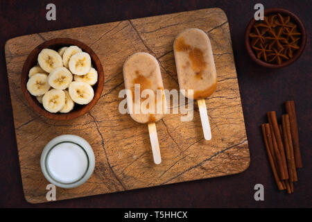 Leckere Bananen Eis Eis am Stiel (Pop) mit Joghurt, Zimt und Caramel (Dulce de Leche Creme) auf einem Marmor Fach. Stockfoto