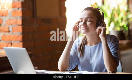 Junge Frau mit Kopfhörern hören Lieblingsmusik sitzen im Innenbereich Stockfoto