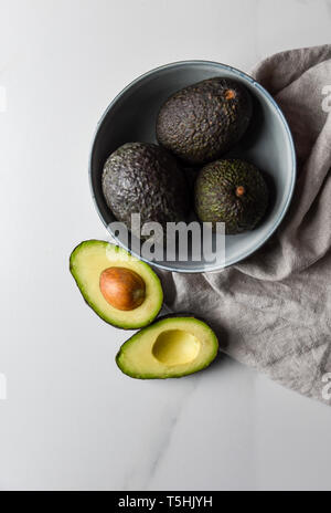 Schüssel mit Avocados mit einem Schnitt in der Hälfte auf einem weißen Arbeitsplatte. Stockfoto