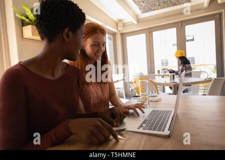 Weibliche Freunde miteinander interagieren, während mit Laptop in einem Cafe Stockfoto
