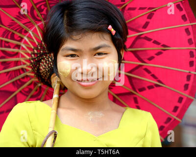 Die burmesische Mädchen mit thanaka Gesicht Kosmetik auf ihren Wangen posiert für die Kamera unter einer traditionellen burmesischen Papier Sonnenschirm.