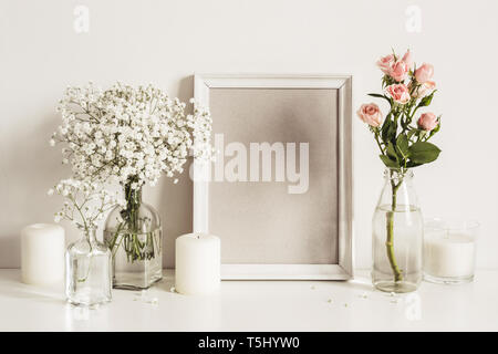 Bilderrahmen, Blumen und Kerzen auf dem Tisch Wand Hintergrund. Vorderansicht mockup Vorlage. Stockfoto