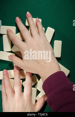 Weibliche Hände mischen domino Knochen auf einen Tisch mit grünem Tuch bedeckt Stockfoto