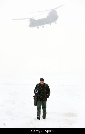 RAF Personal zu Fuß durch den Schnee als Chinook Hubschrauber fliegen Vergangenheit im Hintergrund. Odiham RAF. 13.01.10 Stockfoto