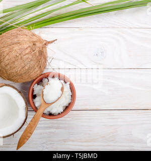 Flach Hintergrund der Kokosnuss, Kokosnussschalen, Öl in Ton Schüssel und Löffel auf weiße Holztisch Stockfoto
