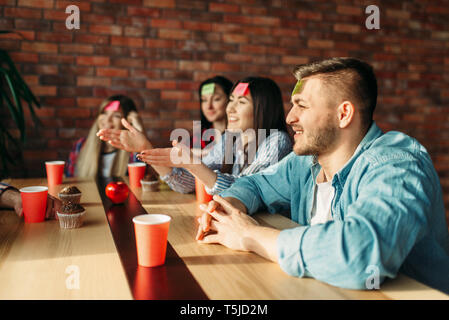 Lächelnd Freunde spielen Aufkleber Hinweise zur Stirn Spiel. Unternehmen spielt, wer ich bin am Tisch im Cafe, denke, das Zeichen Stockfoto