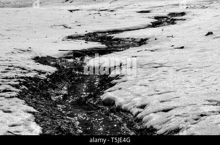 Tauwetter klein im verschneiten Boden in den europäischen Alpen an einem kalten Tag Trickle im Winter von der Sonne hervorgehoben Stockfoto