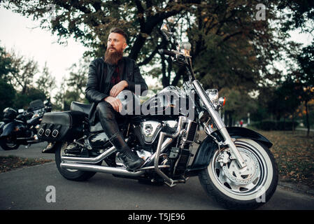 Baerded biker stellt auf der Häckslerwelle, lehnte sich auf einen Helm. Vintage bike, Fahrer und seinem Motorrad, Freiheit Lifestyle, Radtouren Stockfoto