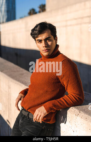 Portrait von modischen jungen Mann mit rollkragen pullover stützte sich auf eine Wand an Sonnenlicht Stockfoto