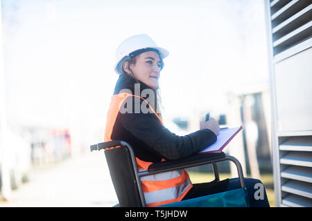 Junge Techniker mit Helm und Weste im Rollstuhl im Freien arbeiten Stockfoto