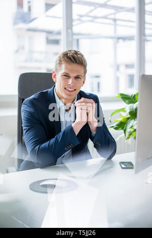 Portrait von selbstbewussten jungen Geschäftsmann am Schreibtisch im Büro sitzen Stockfoto