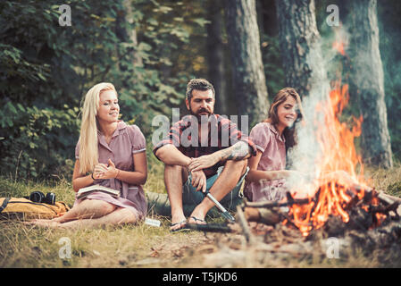 Lächelnd Freunden letzten Sommer Tage im Freien genießen. Jugendliche Sitzen am Lagerfeuer. Mädchen Bücher lesen während der Sitzung auf Gras Stockfoto