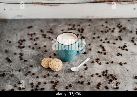 Tasse Milchkaffee, ganze Mahlzeit cookies, Porzellan Löffel und verstreute Kaffeebohnen Stockfoto