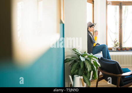Frau sitzt auf der Fensterbank in stilvolles Apartment holding Coffee Mug Stockfoto