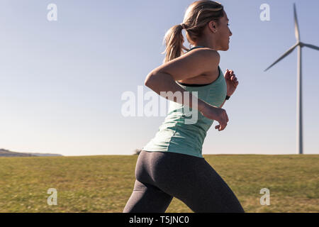 Junge Frau joggen auf Feld weg, wind Räder im Hintergrund Stockfoto