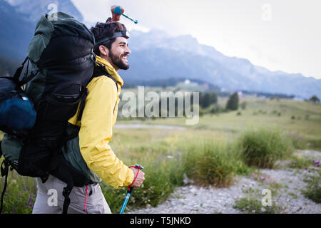 Wanderer junger Mann mit Rucksack und Wanderstöcke mit Blick auf die Berge im Außenbereich Stockfoto