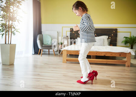 Kleines Mädchen verkleiden, das Tragen der roten High Heels der Mutter Stockfoto