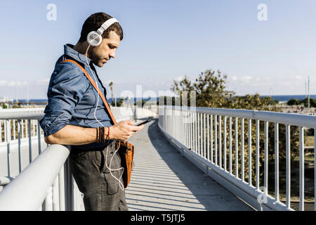 Mann stand am Steg Musik hören mit Kopfhörern und Smartphone Stockfoto