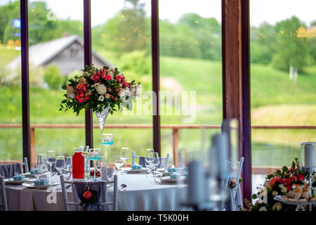 Hochzeit Tischdekoration. Schönen Blumenstrauß in der Vase auf dem Tisch, neben Tellern, Gläsern und Geschenkboxen. Blumenstrauß, Gläser, gif Stockfoto