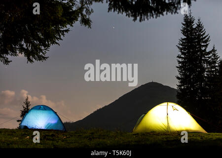 Zwei hell leuchtende, touristische Zelte auf der grünen Wiese Wald Lichtung auf dunklen Berg und dem klaren, blauen Sternenhimmel Kopie Raum Hintergrund. Tourismus, Nacht campin Stockfoto