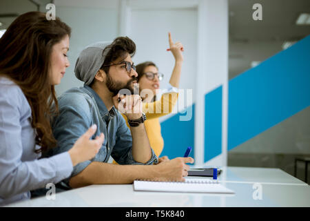 Gruppe von jungen Studenten steigende Hände die Frage während der Schulung in der Werkstatt zu beantworten Stockfoto