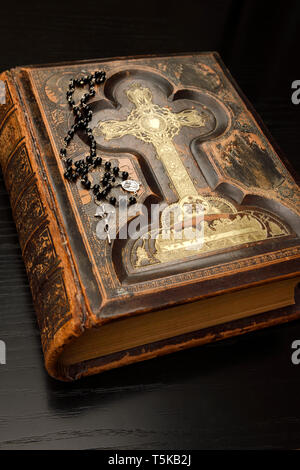 Alte Leder gebunden vergoldete Heilige Bibel mit Rosenkranz auf schwarz Eiche Tisch Stockfoto