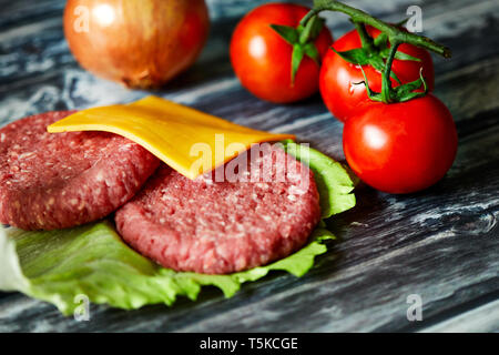 Detail der Hamburger iingredientes wie Cheddar, Rindfleisch, Zwiebeln, Tomaten, Salat in einem dunklen Holz Hintergrund Stockfoto