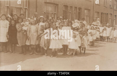 Vintage British photographische Postkarte zeigt eine große Gruppe von vor allem Mädchen Posieren in der Straße mit Bewohnern. Stockfoto