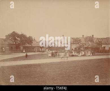 Vintage Edwardian photographische Postkarte zeigen Kinder beim Spielen auf einem Dorfplatz in einem ländlichen Britischen Dorf. Stellmacher Arbeiten im Hintergrund. Stockfoto