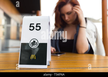 RIGA, Lettland - 22 April, 2019: Warten auf Bestellung und denken über Ihr Gewicht - junge Frau Essen in Fast-Food-Restaurant Mcdonalds Stockfoto