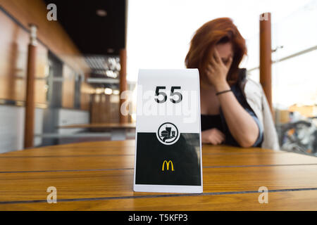 RIGA, Lettland - 22 April, 2019: Warten auf Bestellung und denken über Ihr Gewicht - junge Frau Essen in Fast-Food-Restaurant Mcdonalds Stockfoto