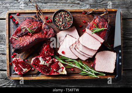 Glasierte smoked Grill Schweinefilet auf eine unhöfliche Holz Schneidebrett mit frischen Granat Samen, Pfefferkörner und Messer, horizontale Ansicht von abov geschnitten Stockfoto