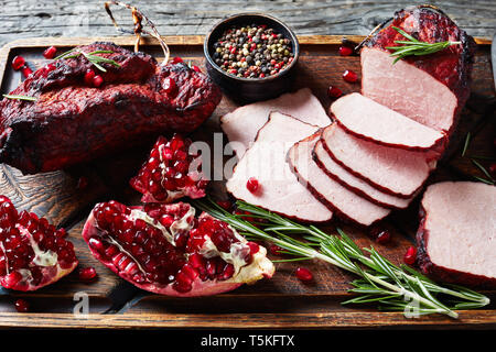 Glasierte smoked Grill Schweinefilet auf eine unhöfliche Holz Schneidebrett mit frischen Granat Samen, Pfefferkörner, horizontale Ansicht von oben, ganz in der Nähe U-Scheiben geschnitten Stockfoto