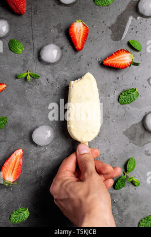 Hand mit Erdbeereis über den Marmortisch mit Erdbeer, Minze und Eiswürfel eingerichtet, Flach, Ansicht von oben Stockfoto