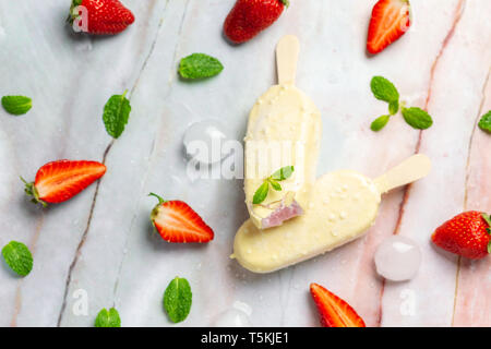 Erdbeer Eis auf Sticks mit weißer Schokolade auf weißem Marmor Stockfoto